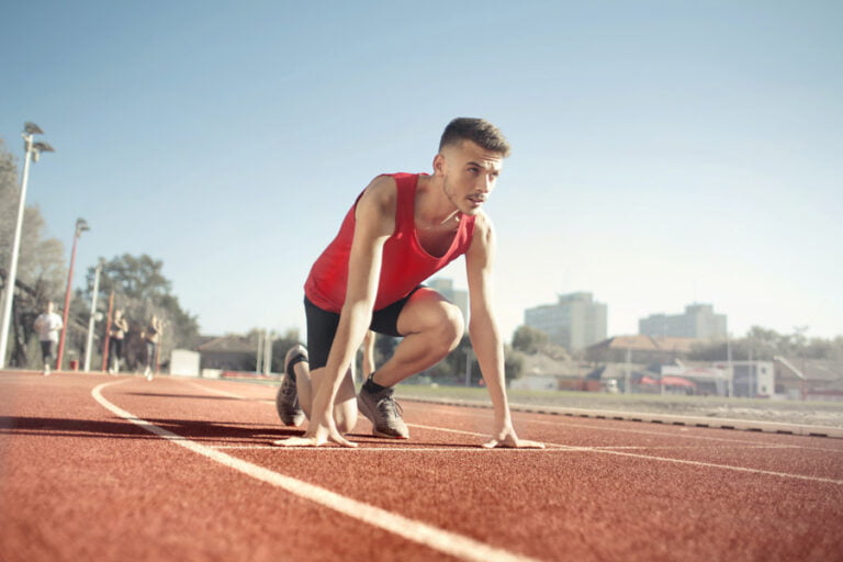 En man med bestämd blick som står i startblocken på en löparbana, med hög motivation att göra ett riktigt bra lopp
