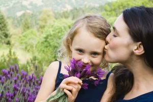 Kvinna som kysser sitt barn med tacksamhet, som i sin tur luktar på blommor